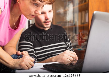 Middle aged woman and young man using laptop at home.