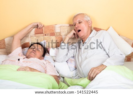 Sleepy senior man and woman yawning in bed