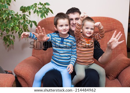 Happy children boys and daddy waving and sitting on sofa at home