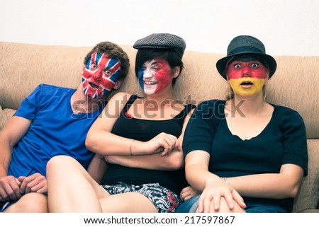 Group of funny people with painted flags on their faces and sitting on sofa.