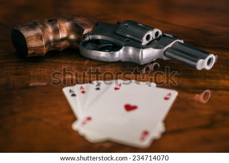 Risky gambling concept. Gun and playing cards on wooden table.