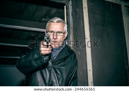Dangerous senior man aiming a gun at you and standing in old dark cabin.