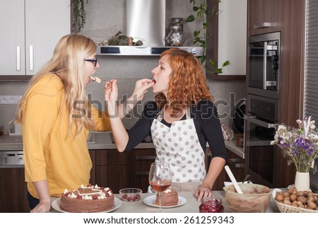 Girlfriends feeding each other with a cake and cooking together in the kitchen at home.