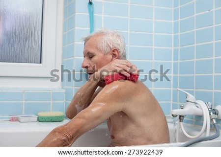 Senior man washing his body with soap sponge in bath.