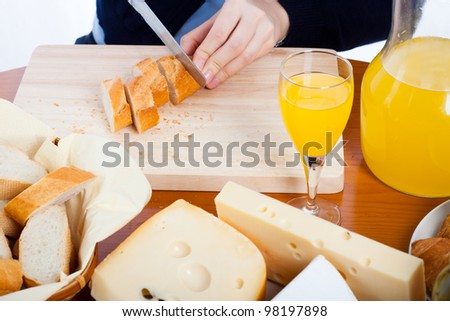 Detail of table with cheese, bread, juice and female hands cutting bread.
