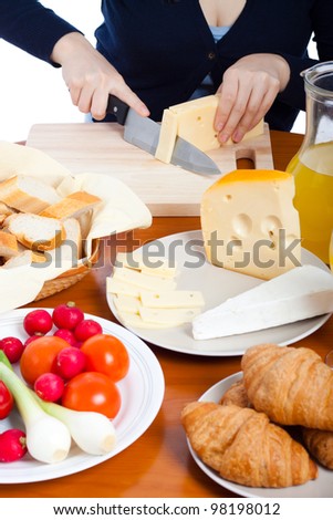 Detail of kitchen table with fresh food and female hands cutting emmenthal cheese.