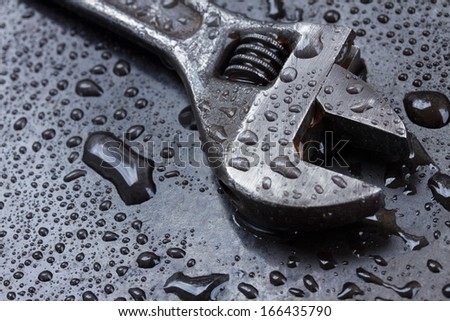 Adjustable spanner on black metal in water drops close up Adjustable spanner on black metal in water drops close up