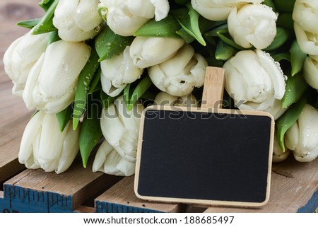 bunch  of fresh white  tulips on wooden table with black  empty chalk board