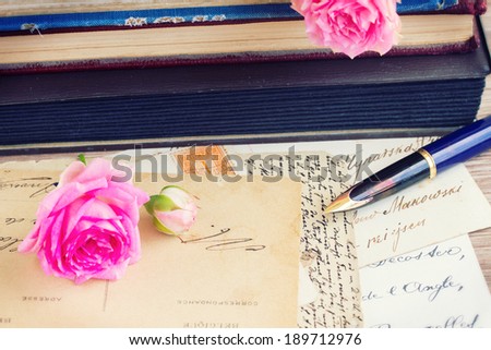 old golden quill pen and antique letters on table with books and roses