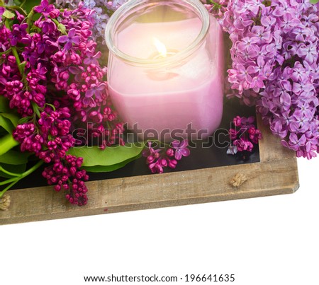 fresh violet lilac flowers with burning candle border on white background