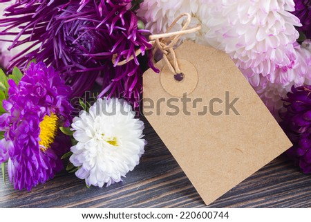 white and violet aster flowers with paper tag  close up  on wooden table