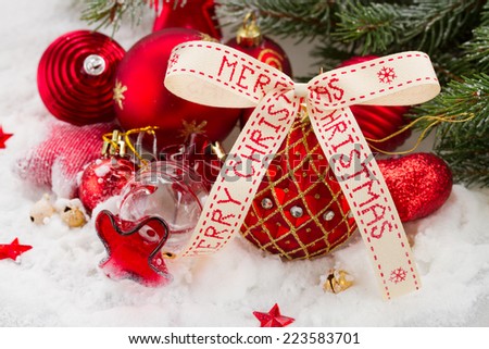 red  and gold christmas ball with merry christmas ribbon  in snowfall under fir tree