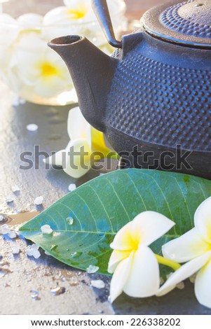 Spa and wellness setting with natural sea salt,flowers and teapot on black stone