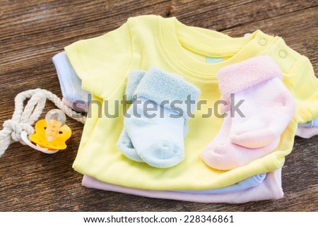 pile newborn baby clothes with  pacifier on wooden background