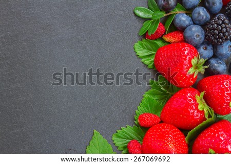 brder  of fresh  wild berries and  leaves with copy space  on black stone background