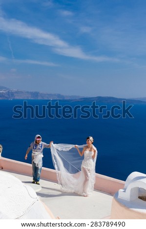 SANTORINI - GREECE on 8 of MAY 2014: Photographer styling bride for wedding photoset against blue Aegan Sea, Oia, Santorini, Greece on 8 may, 2014