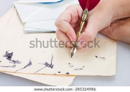 someone hand holding red feather pen  over old papers with ink blots