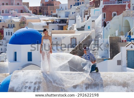 SANTORINI - GREECE on 8 of MAY 2014: Photografer styling bride for wedding photoset against blue Aegan Sea, Oia, Santorini, Greece on 8 may, 2014