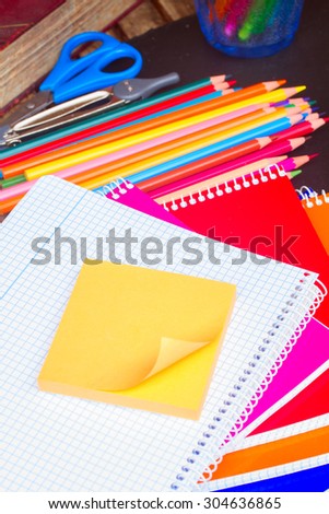 Empty notebook with orange sticker and set  of colorful pencils on black board
