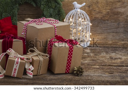 Handmade paper gift boxes on wooden background with evergreen wreath and lights