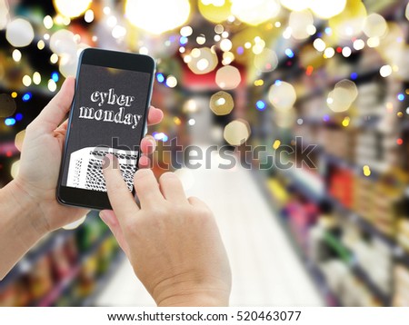 someones hands holding mobile smart phone with mobile shop on supermarket blur background and shopping bags - cyber monday e-commerce concept