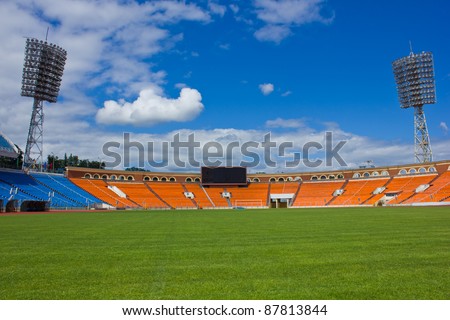 football field with seats, lights, scoreboard and green grass