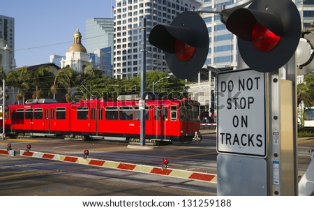 Downtown Scene at RailRoad Crossing Red Trolley Car Passing Signal Lights with Buildings in the Background