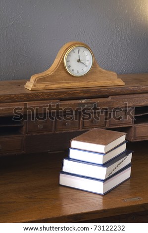 Hardcover Books sit atop on Antique Wood Roll-top Desk with Mantle Clock in Vertical Composition