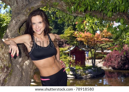 Beautiful Brunette Woman Wearing Spandex Pants Sports Bra Standing by tree Outdoors
