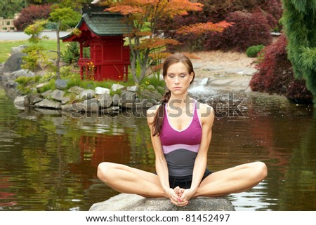 Woman Doing Yoga Eyes Closed Meditation Sitting on Rock Pagoda Pond