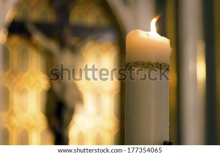 decorated white candle burning inside a Catholic with the image of Christ behind Church