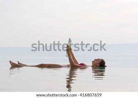 girl reading a newspaper floating in the waters of the Dead Sea