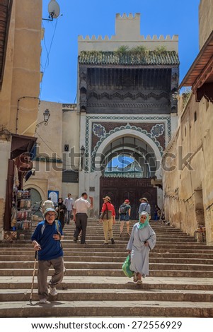 Fes, Morocco - May 11, 2013: Locals and tourists walking in the medina in Fes, on the steps leading to an ornate gate decorated with mosaic
