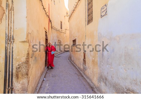 Fes, Morocco - May 11, 2013: Woman wearing a kaftan, traditional Moroccan clothing, stepping out into a narrow street in Fes Medina in Morocco