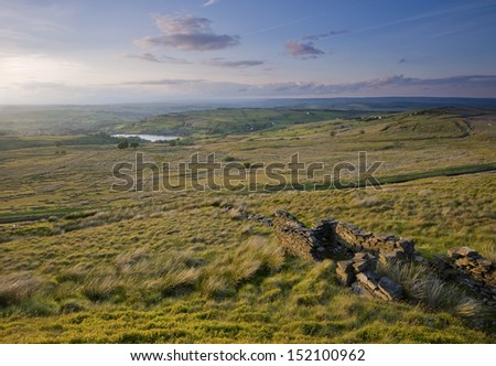 A late afternoon sunset in summer lights up the green moorland grasses and dry stone walls over a classic yorkshire dales scene