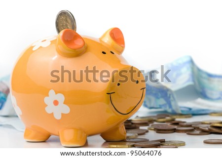 ceramic piggy money box sorounded by spanish official currency. euro coins and banknotes