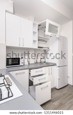 Modern white and black kitchen, gas stove, some drawers and lockers are open