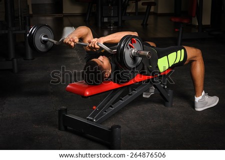handsome young african descent mixed race man doing bench french press workout with barbell in gym