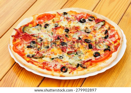 Whole pizza with cut pepperoni, black olives, corn, cheese and pickled cucumbers