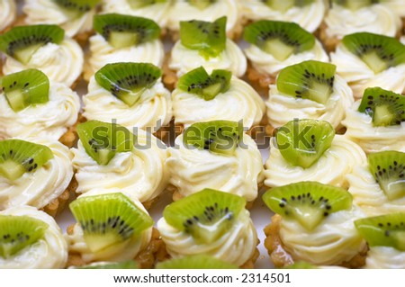 Small cakes (petit four) with custard and kiwi on top. Shallow DOF. Sharp focus on second line.
