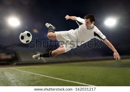 Soccer player jumping and kicking the ball inside a stadium at night - stock photo