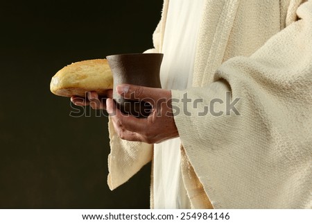 Jesus holding bread and a cup of wine isolated on a dark background