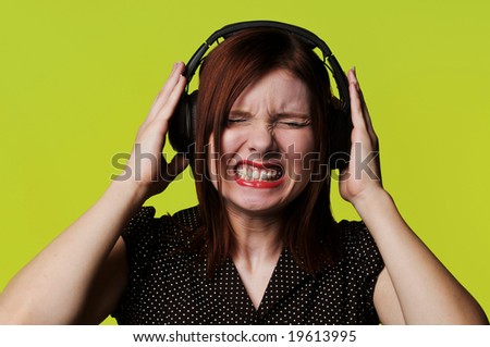 Young woman with headphones listening to loud music against a green background