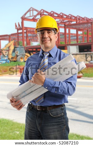 Portrait of engineer at construction site holding plans and wearing hard hat