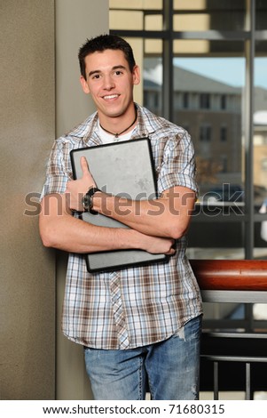 Young man holding his laptop computer with college buildings as background