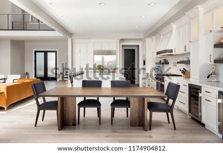 Beautiful dining room and kitchen in new luxury home with partial view of living room and entry. Has dining room table, stainless steel appliances, hardwood floors, and waterfall island.