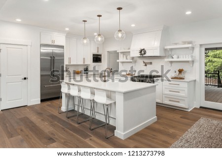 beautiful white kitchen in new luxury home with island, pendant lights, hardwood floors, and stainless steel appliances