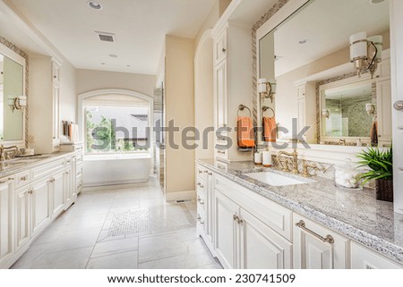 Large bathroom interior in luxury home with two sinks, tile floors, fancy cabinets, large mirrors, and bathtub