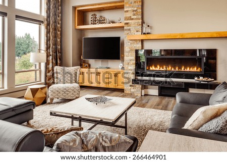Home living room with hardwood floors, fireplace with roaring fire, coffee table, and mantle in new luxury house