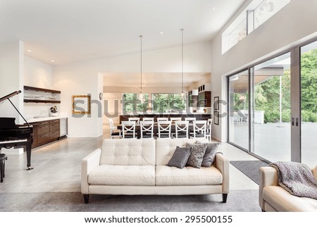 Beautiful living room in new luxury home with couch, piano, sliding glass doors leading out to backyard patio, huge dining room table, pendant lights, vaulted ceilings, wet bar, and kitchen